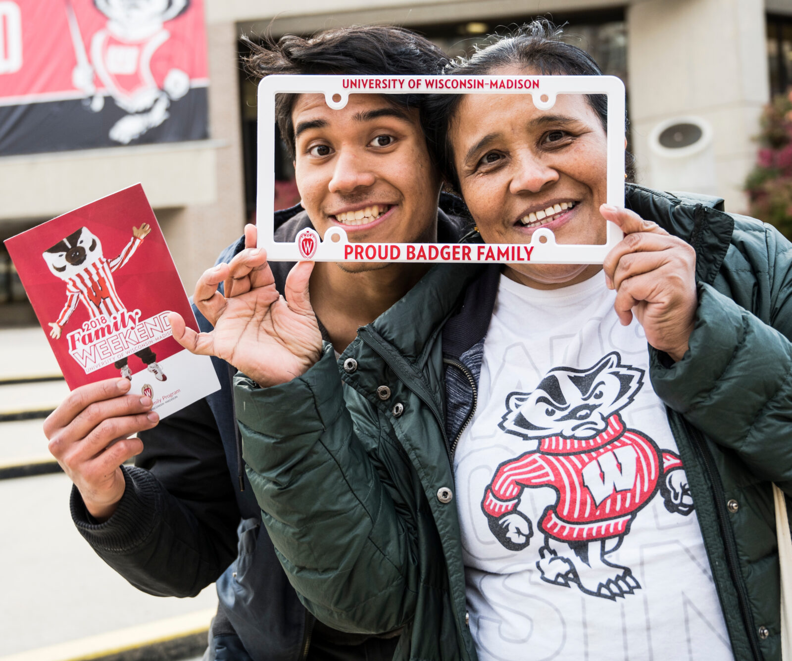 UW-Madison student poses for a photo with his mother through a "Proud Badger Family" license plate cover, during a Family Weekend welcome event held at Union South at the University of Wisconsin-Madison.