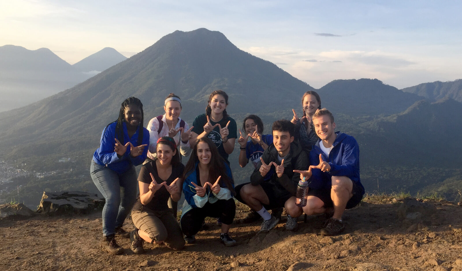 Students hold up the motion W in front of a mountain range in Guatemala during a study abroad trip.