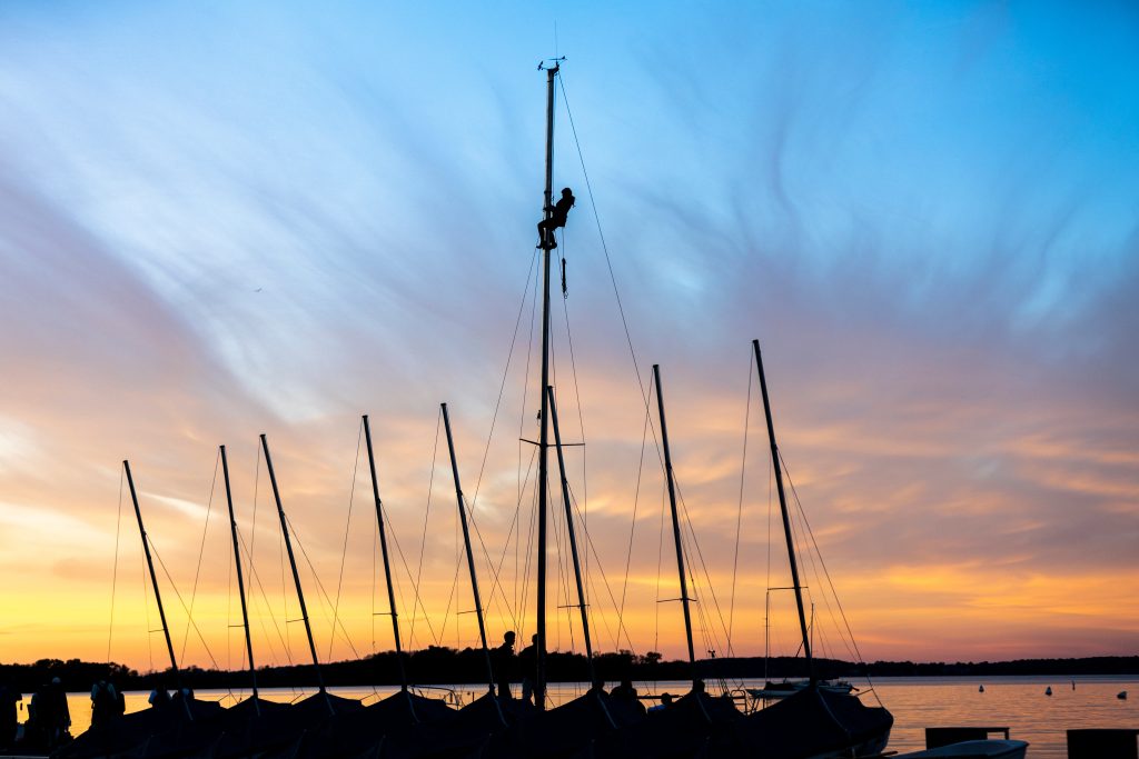 A person climbs a sailboat’s mast on Lake Mendota during sunset near Memorial Union at the University of Wisconsin–Madison during a mild autumn day.