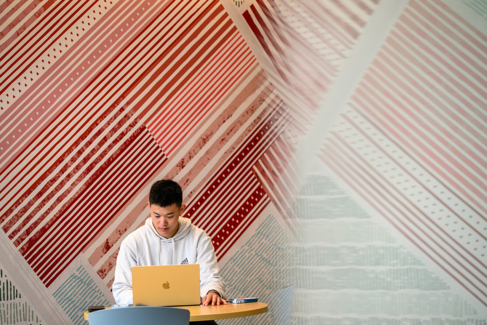 A student sits with his laptop in front of a red and white striped wall