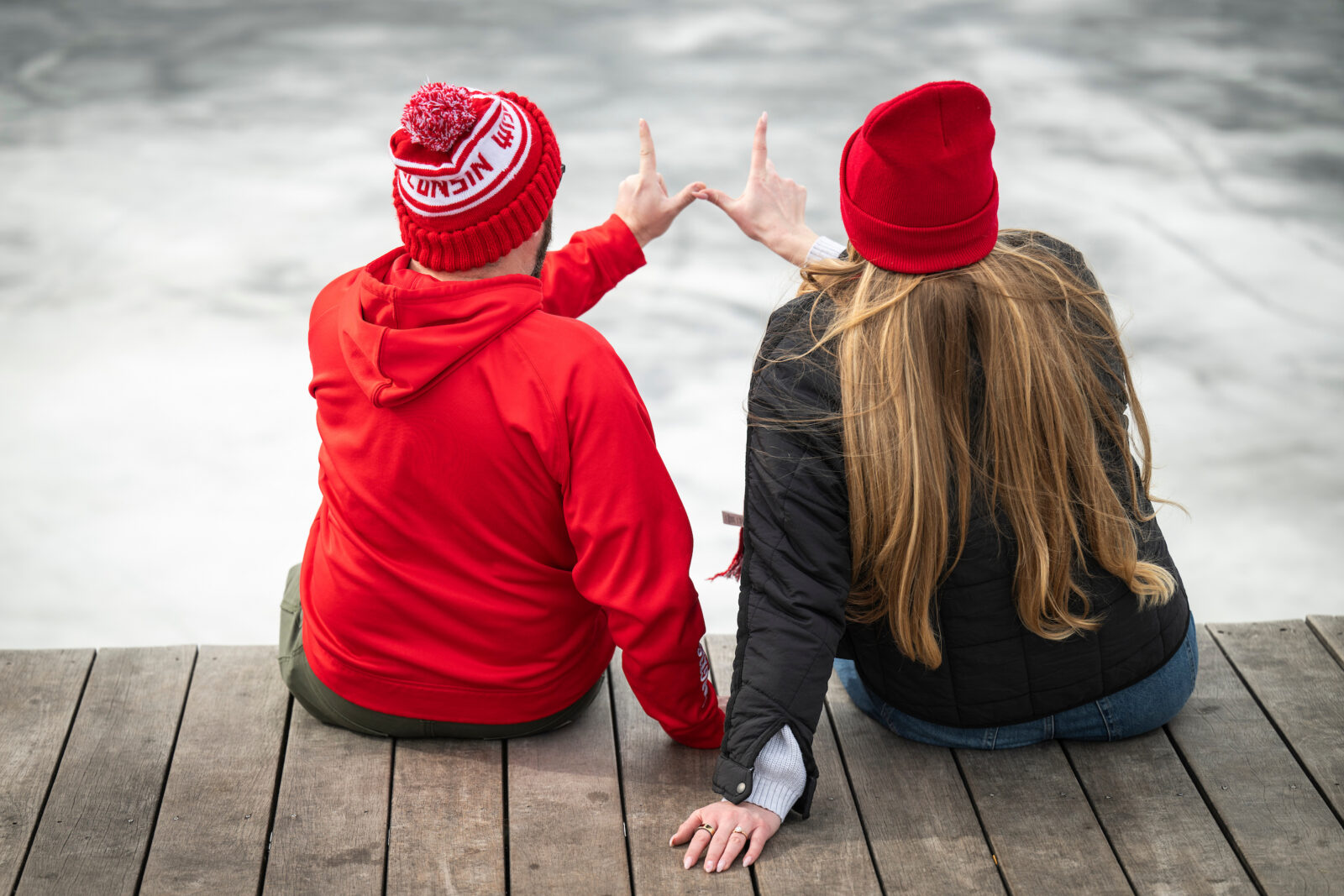 Two people, decked out in Wisconsin Badger hats, make a W with their hands on the Goodspeed Family Pier
