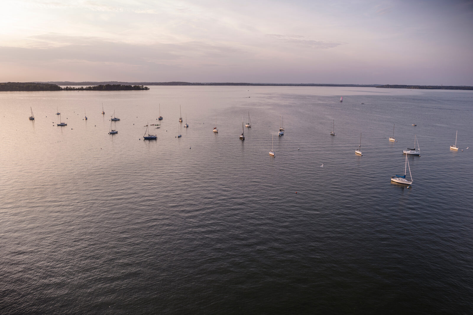 Sailboats are moored on Lake Mendota near the Memorial Union Terrace with Picnic Point seen in the background