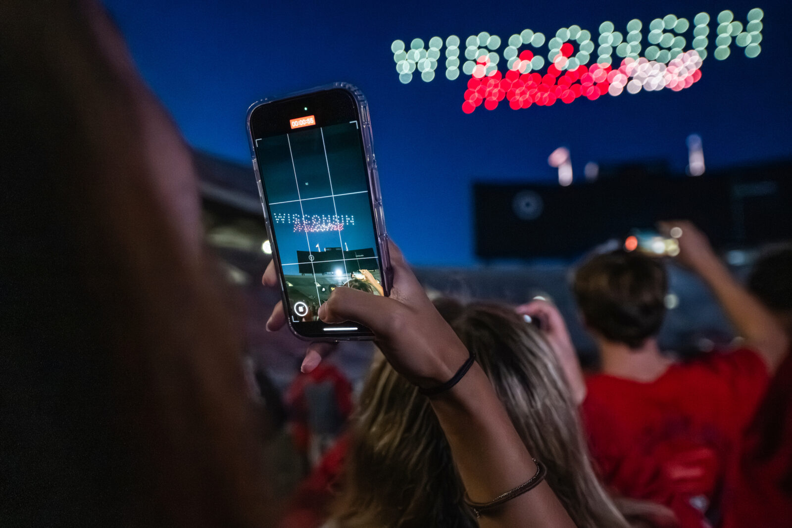 A student films the drone show on their cell phones spelling "Wisconsin Welcome"